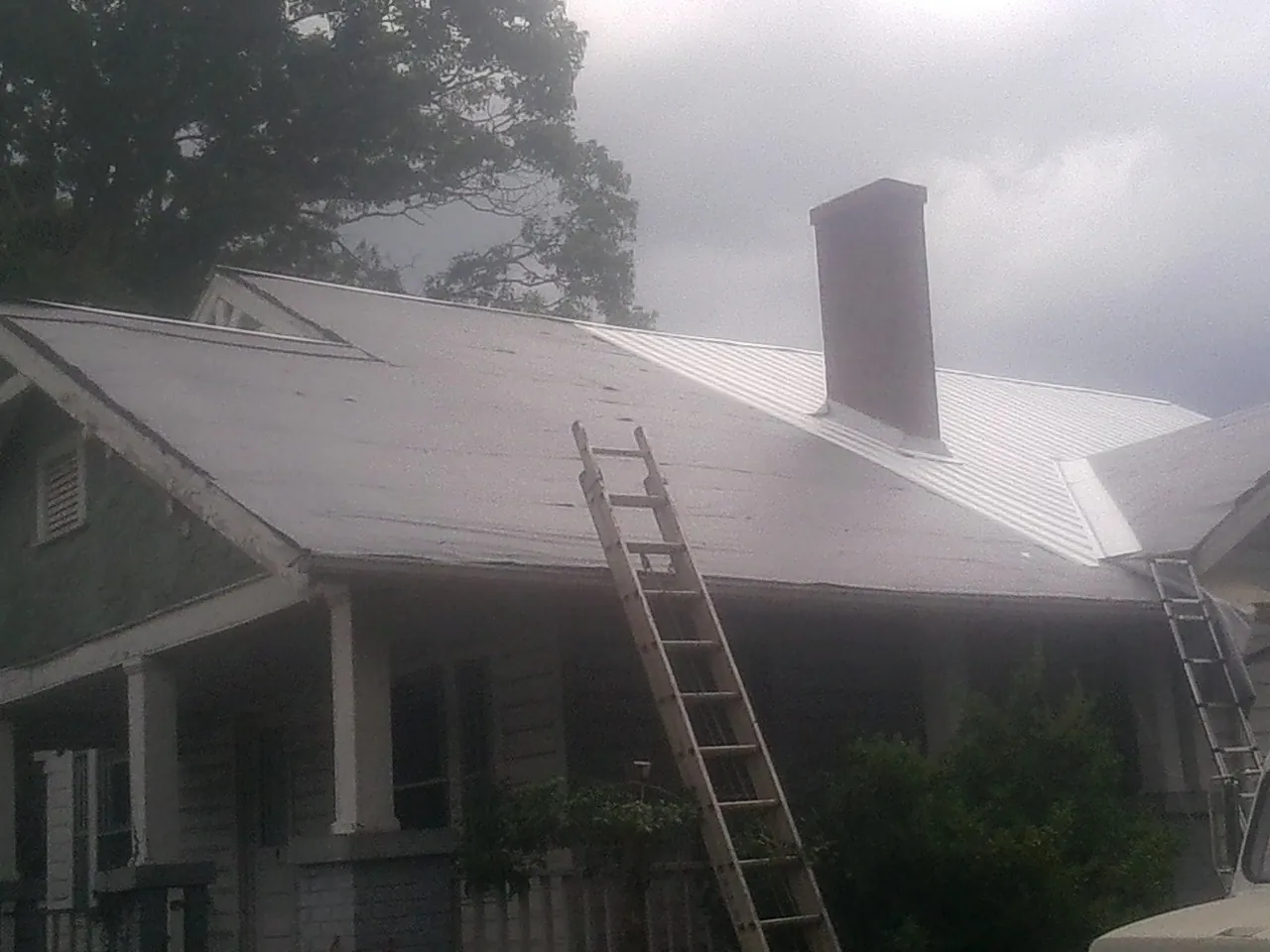 Ladders against a metal roof on an older home with a brick chimney in Orderville