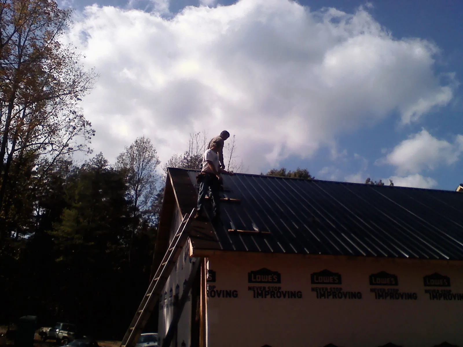 Roofer fastening dark metal panels high against a cloudy sky, from a Roof Inspection job in Orderville